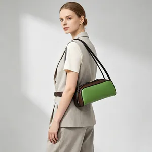 Modelo luciendo un bolso de hombro baguette minimalista bicolor en verde y marrón