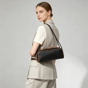 Vista lateral de un bolso baguette negro con ribete marrón llevado por una modelo