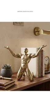 Artistic golden resin figurine kneeling on a wooden desk with books in background