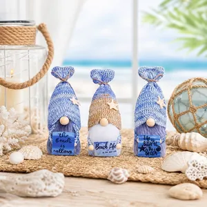 Three knitted ocean-themed beach gnomes holding signs on a shell-decorated mat