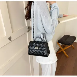 Détail d'un sac à bandoulière noir tressé porté avec un pull en maille bleu clair