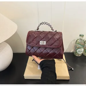 Détail d'un sac bandoulière tressé bordeaux avec fermoir rotatif argenté et bandoulière chaîne