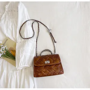 Sac à main vintage en cuir tressé marron avec chaîne argentée sur fond de robe blanche