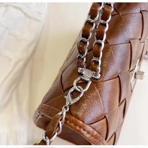 Détail d'un sac à main tissé marron avec bandoulière en chaîne argentée et texture.