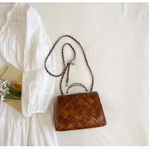 Détail d'un petit sac bandoulière marron tressé rétro posé sur une robe blanche chic