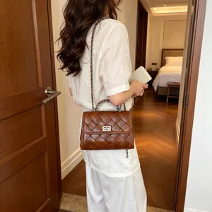 Sac à main carré matelassé marron élégant avec bandoulière chaîne porté par un modèle en intérieur