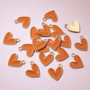 Detail of orange enamel heart charms with gold beaded edges for DIY jewelry making.