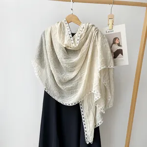 Close-up detail of a beige cotton linen scarf with elegant white lace embroidery.