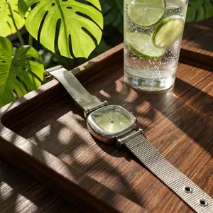 Close-up of minimalist square green dial watch with silver mesh strap on wooden tray
