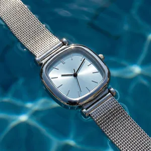 Close-up of a silver square lady watch with mesh strap on rippling blue water background