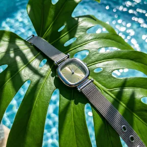 Close-up of minimalist square ladies watch with silver mesh strap on green leaf