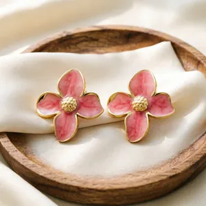 Gros plan de boucles d'oreilles fleurs roses en émail présentées sur de la soie blanche.
