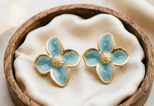 Gros plan sur des boucles d'oreilles fleur à quatre pétales en émail bleu et or