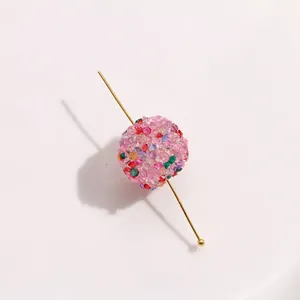 Primo piano di una perla a sfera in resina colorata e scintillante con spillo dorato per fai-da-te.
