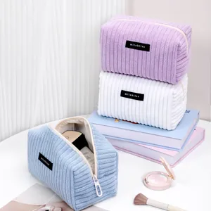 Three colorful corduroy makeup bags in pastel purple, white and blue colors
