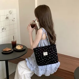 Dettaglio borsa tote in velluto nero con fiocchi bianchi e cuori in un caffè