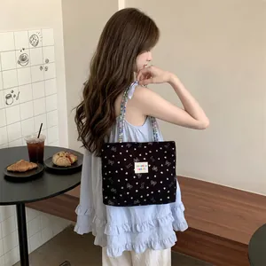 Vista dettagliata di una borsa tote in velluto nero con motivi a fiocco indossata da una modella.