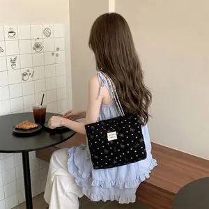 Vista lifestyle di una borsa tote nera in velluto a coste con motivi a cuore e fiocchi al caffè.