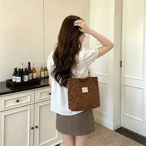 Foto lifestyle di una borsa tote in velluto a coste marrone con motivi a fiocco neri.