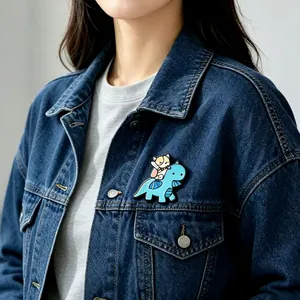 Detail shot of a cute cartoon dinosaur and cat enamel pin on a blue denim jacket