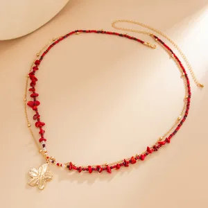 Detailed shot of a double-layered body chain with red beads and a golden flower pendant.