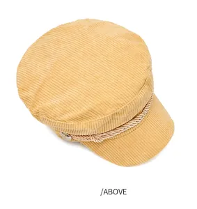 Close-up top view of a mustard yellow corduroy baker boy hat with decorative rope trim