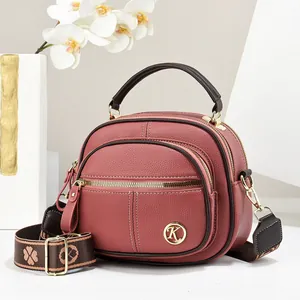 Close-up of pink round crossbody bag with gold hardware and wide patterned strap