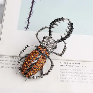 Vintage kever broche met oranje en zwarte steentjes op een tijdschrift achtergrond.