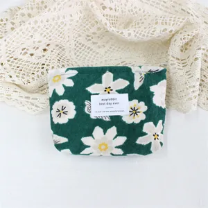 Close-up of a green floral corduroy cosmetic pouch with a white label on lace fabric.