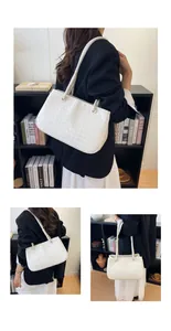 Lifestyle detail shot of a white woven shoulder bag carried by a model in a black blazer