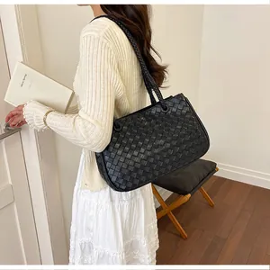 Detail view of a black woven leather tote bag carried on a woman's shoulder.
