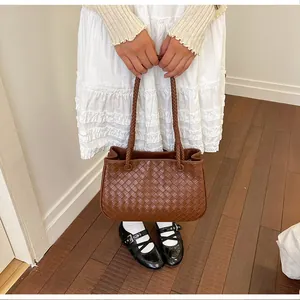Close-up of a stylish brown woven handbag held by a model wearing a white dress