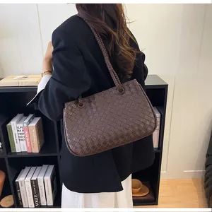 Close-up of a dark brown woven leather tote bag worn by a model in a stylish office setting.