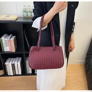 Close-up detail of a wine red woven leather shoulder bag held by a model in a black blazer