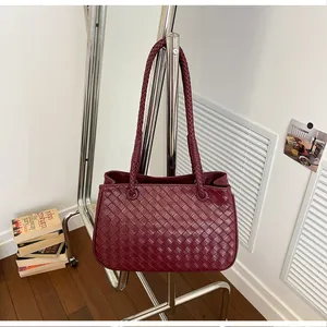 Elegant burgundy woven leather shoulder bag with Intrecciato pattern hanging on a rack
