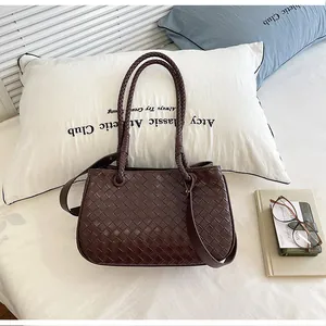 Detail showing dark brown woven leather shoulder bag on minimalist white bedding