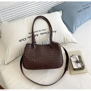 Detailed view of a brown woven shoulder bag on a white bed with lifestyle decor props