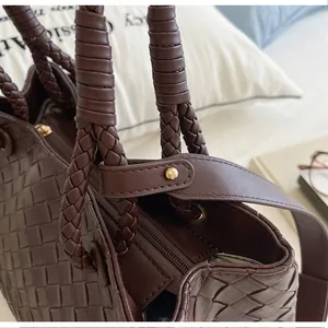 Detail of brown woven bucket bag featuring braided leather handles and gold stud.