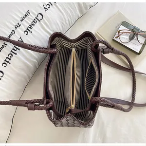 Interior detail of a brown woven handbag with striped lining and zipper divider