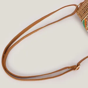Primo piano dettagliato della tracolla in ecopelle marrone su una borsa intrecciata colorata