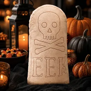 Close-up view of a tombstone plush pillow featuring skull embroidery and EEK lettering