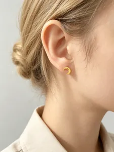 Detailopname van een minimalistische gouden halve maan oorknopje op de oorlel sieraden