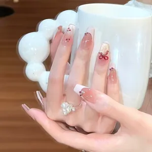 Detail view of elegant pink press-on nails with cherry motifs and 3D red bow design.