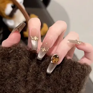 Close-up detail of gray cat-eye press-on nails with amber rhinestone accents