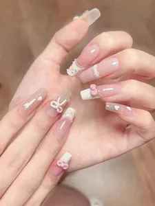 Close-up detail of elegant pink press-on nails with 3D white bows and pearl accents
