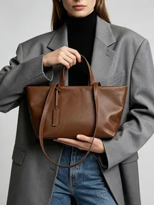 Vista detallada de un bolso tote de cuero marrón llevado por una modelo con americana.