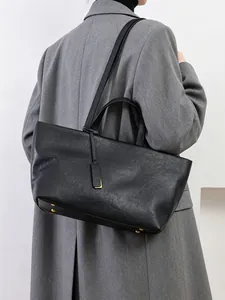 Mujer en blazer gris llevando un gran bolso tote negro de cuero suave al hombro
