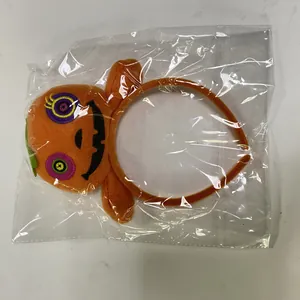 Detail view of a plush Halloween pumpkin headband inside a clear plastic package