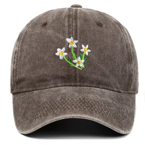 Detailweergave van de bruin gewassen katoenen baseballpet met witte bloemenborduur.