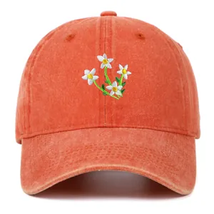 Detailopname van delicaat wit bloemborduursel op een vintage gewassen oranje baseballpet.